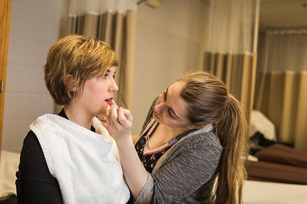 A cosmetology student applies makeup to a woman's face