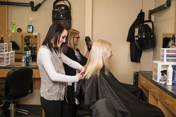 A cosmetology student cuts a blonde woman's hair