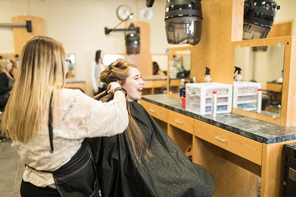 A cosmetology student works on a woman's curled hair
